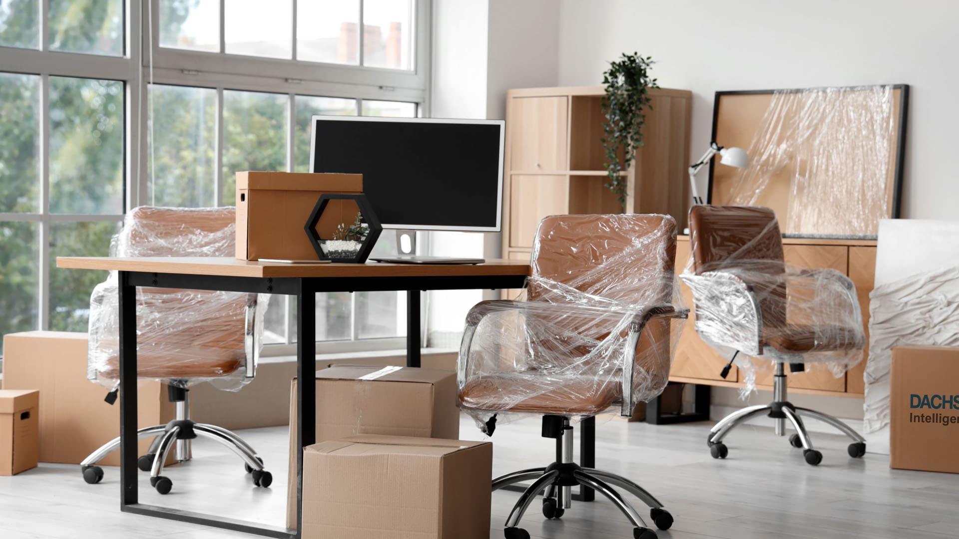 Verpackte Bürodrehstühle, Schreibtisch und Kartons in hellem Büro beim Umzug