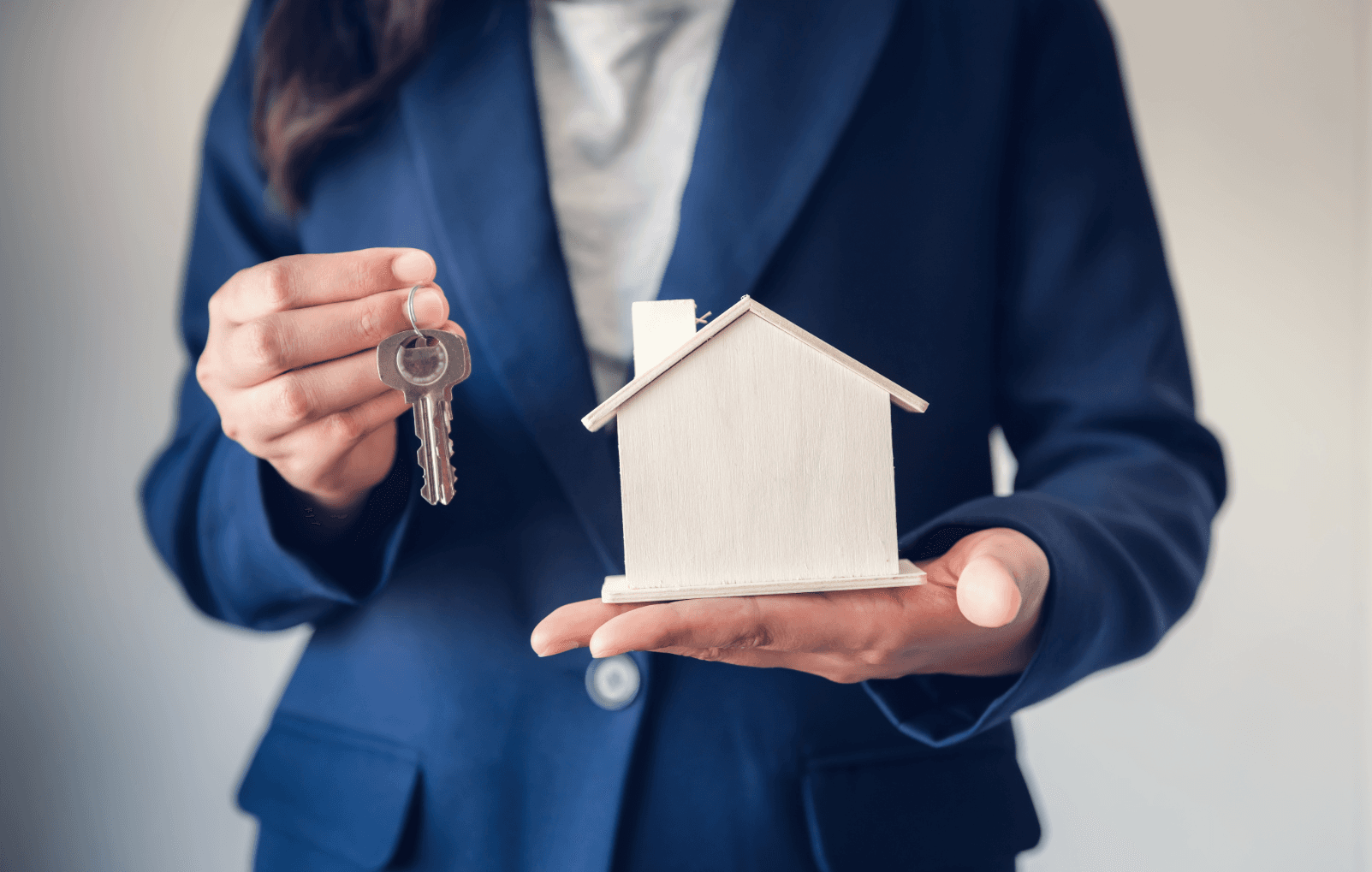 Person übergibt Schlüssel und Modellhaus – symbolische Darstellung einer Wohnungsübergabe